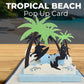 Tropical beach 3D pop-up card with surfers riding waves beneath green palm trees