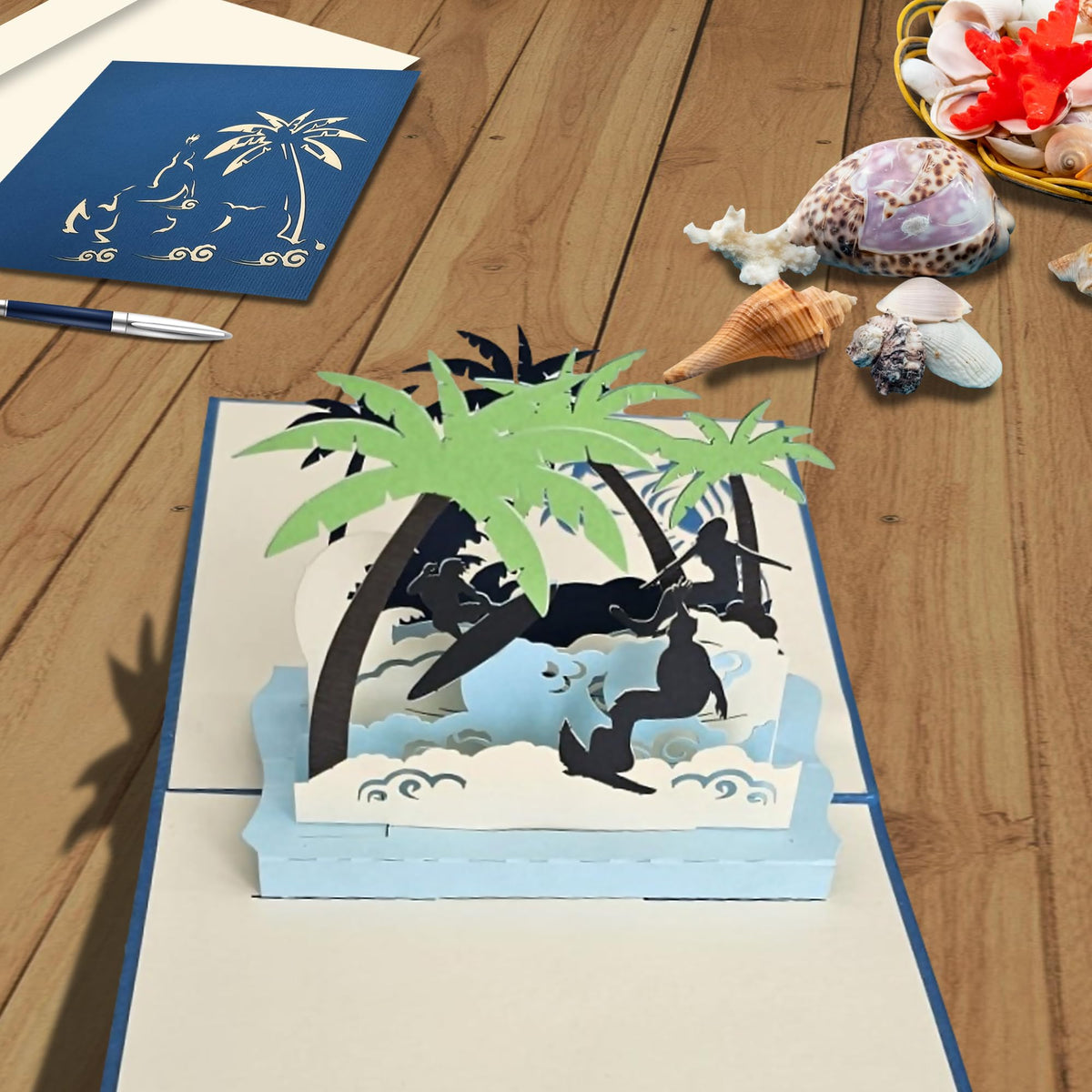 Surfing pop-up greeting card displayed open on a table with blue cover and envelope